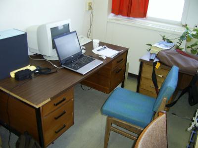 Ein Tisch, ein alter Computer, ein Stuhl und mein Laptop.